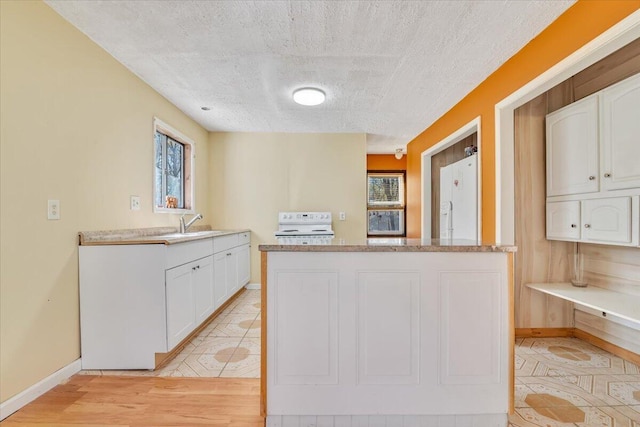 kitchen featuring a textured ceiling, a sink, baseboards, white appliances, and white cabinetry