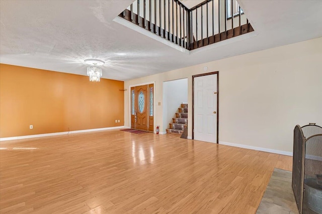 unfurnished living room featuring baseboards, stairs, wood finished floors, and a chandelier