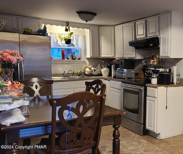 kitchen featuring dark countertops, stainless steel appliances, under cabinet range hood, a sink, and light tile patterned flooring