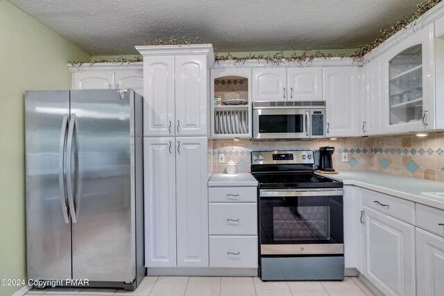 kitchen featuring backsplash, glass insert cabinets, light countertops, stainless steel appliances, and white cabinetry