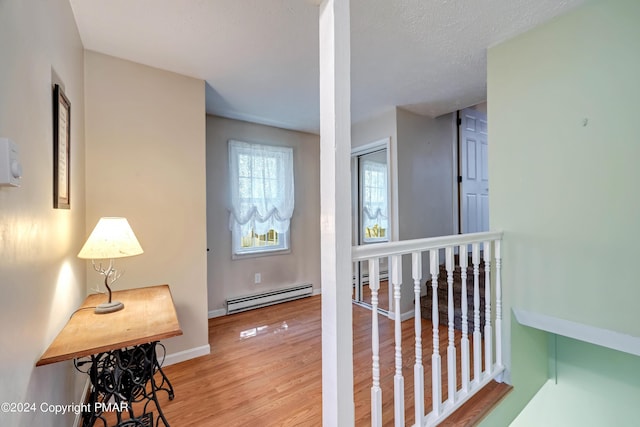 hallway with baseboard heating, a textured ceiling, baseboards, and wood finished floors