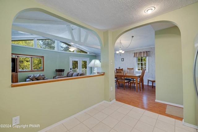 hall featuring tile patterned floors, a textured ceiling, an inviting chandelier, baseboards, and vaulted ceiling with beams