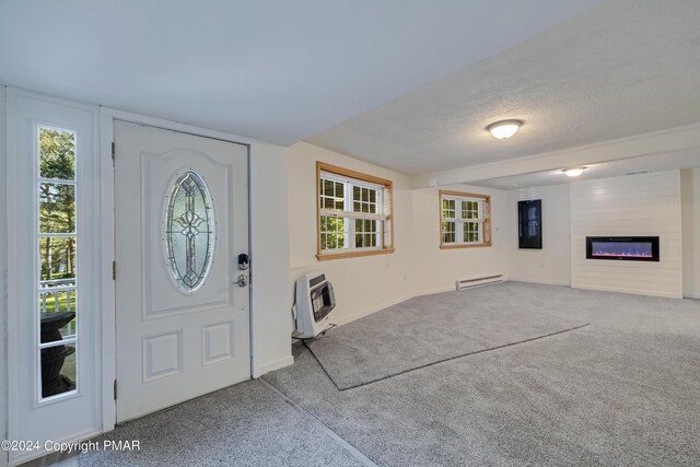 carpeted foyer entrance featuring heating unit, a textured ceiling, a glass covered fireplace, baseboards, and baseboard heating