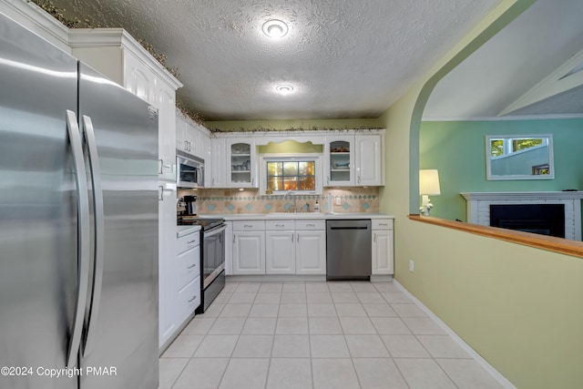 kitchen with backsplash, glass insert cabinets, light tile patterned floors, stainless steel appliances, and white cabinetry