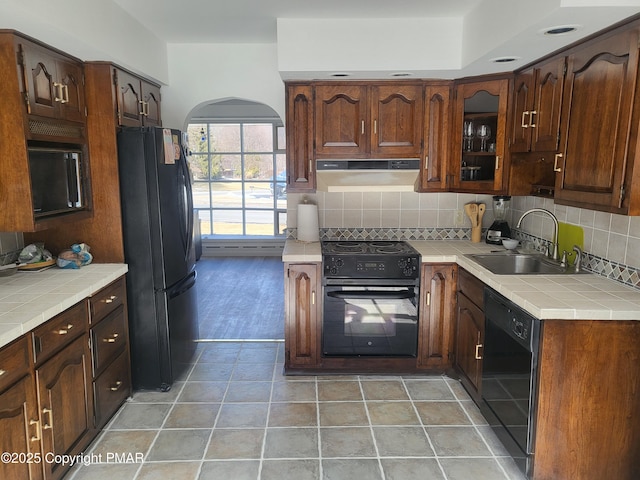 kitchen with tile countertops, arched walkways, a sink, decorative backsplash, and black appliances