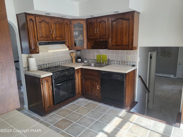 kitchen featuring arched walkways, under cabinet range hood, a baseboard heating unit, a sink, and black appliances