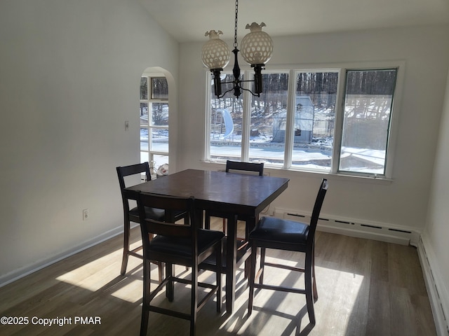 dining area featuring arched walkways, a notable chandelier, a baseboard radiator, wood finished floors, and baseboards