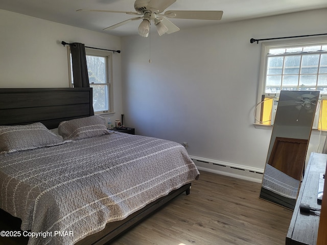 bedroom featuring a ceiling fan, baseboard heating, and wood finished floors