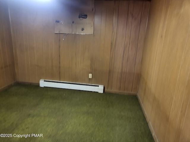 empty room with wood walls, carpet, a baseboard heating unit, and baseboards