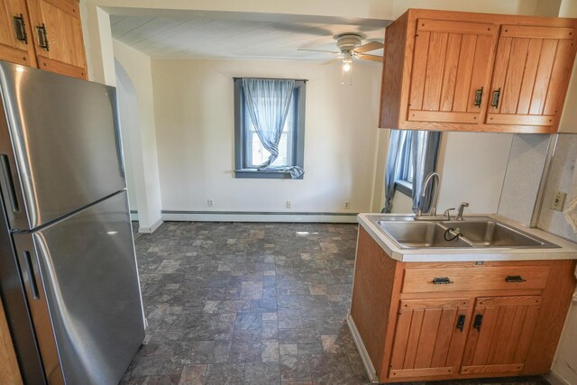 kitchen featuring freestanding refrigerator, a ceiling fan, stone finish floor, a baseboard heating unit, and a sink