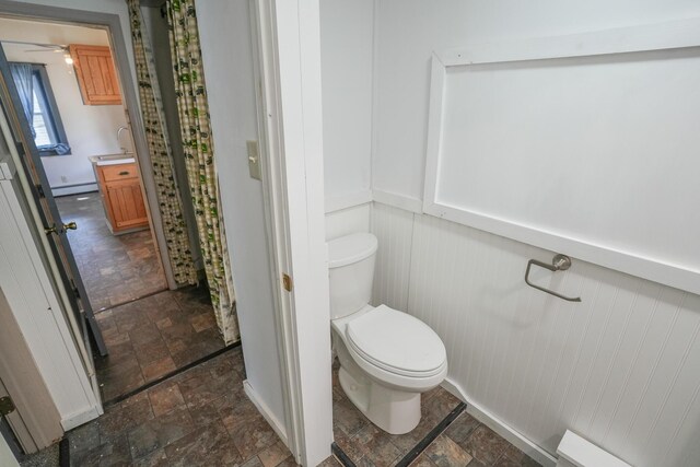 bathroom with a sink, stone finish flooring, a baseboard heating unit, and toilet