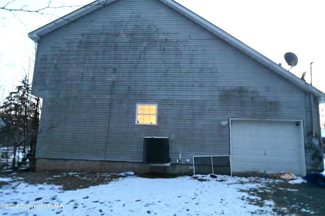 view of snow covered exterior with a detached garage and central AC unit