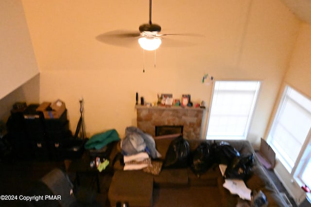 living area featuring ceiling fan and a stone fireplace