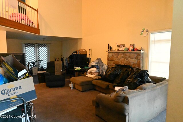 living area with carpet, a stone fireplace, and a high ceiling