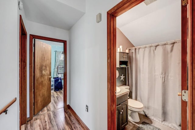 full bath featuring wood finished floors, vaulted ceiling, toilet, vanity, and baseboards