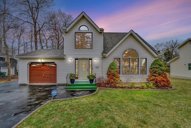 traditional home with a garage, a shingled roof, driveway, and a front yard