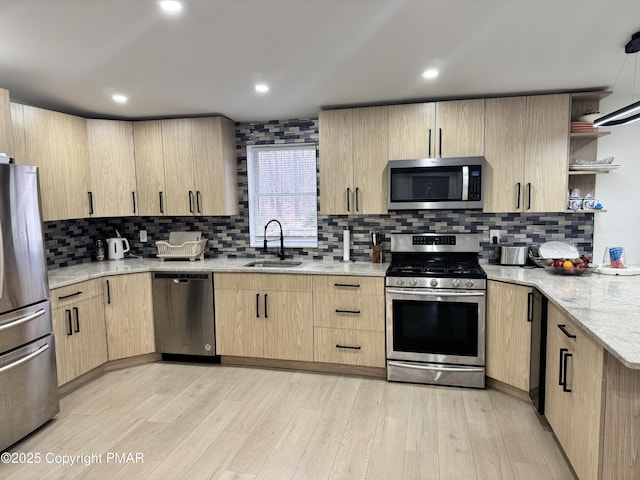 kitchen with light stone counters, light brown cabinets, stainless steel appliances, a sink, and light wood-type flooring