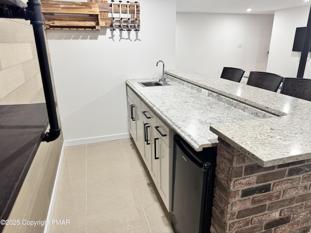 kitchen with light stone counters, white cabinetry, a sink, a peninsula, and baseboards