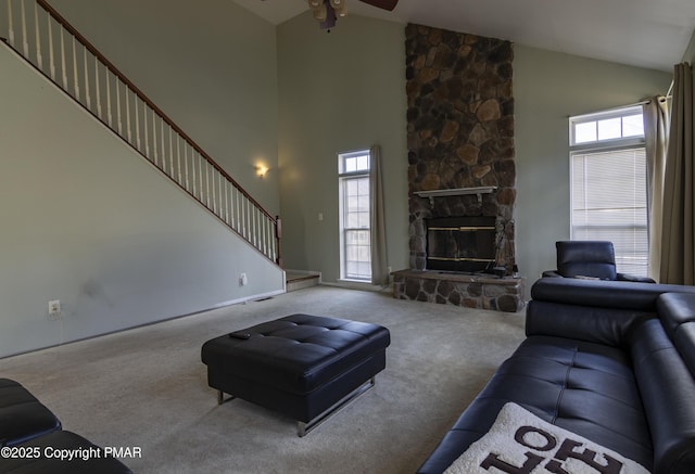 carpeted living room with ceiling fan, high vaulted ceiling, a stone fireplace, and stairway