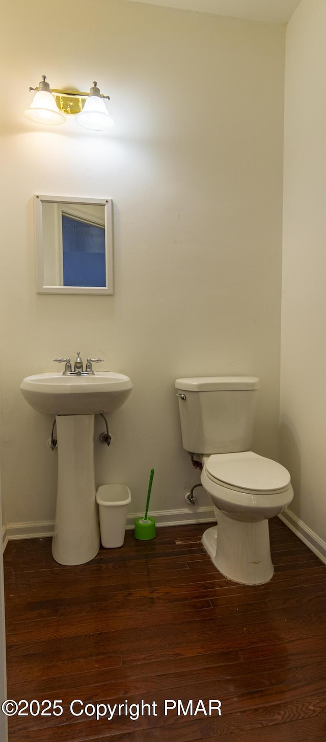 half bath with a sink, wood finished floors, toilet, and baseboards