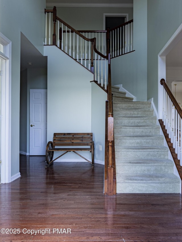 staircase featuring wood finished floors, a towering ceiling, and baseboards