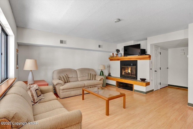 living area featuring a textured ceiling, visible vents, wood finished floors, and a glass covered fireplace