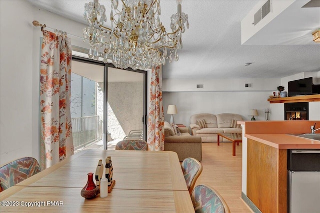 dining space with visible vents, a textured ceiling, and light wood finished floors