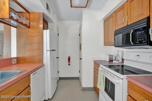 kitchen featuring light countertops, brown cabinetry, a sink, white appliances, and baseboards