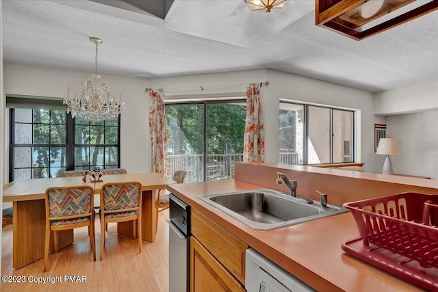 kitchen with light countertops, light wood-style floors, brown cabinetry, a sink, and a chandelier