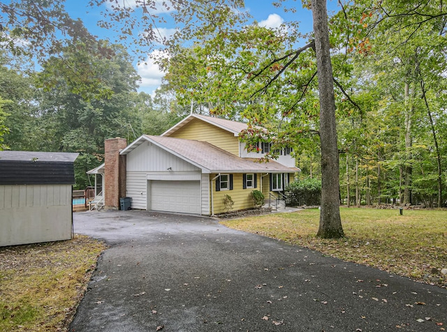 view of front of home featuring a front lawn, aphalt driveway, a storage shed, an attached garage, and a shingled roof