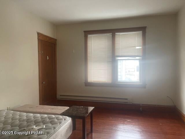 bedroom featuring a baseboard heating unit, wood finished floors, and baseboards