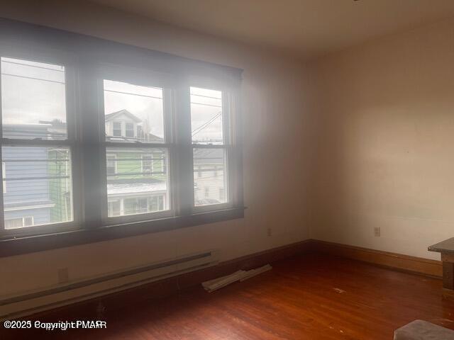 spare room with a baseboard radiator, wood finished floors, and baseboards