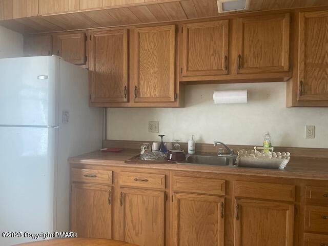 kitchen with visible vents, brown cabinets, freestanding refrigerator, light countertops, and a sink