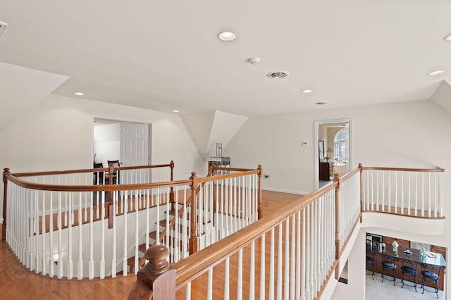 corridor featuring lofted ceiling, visible vents, recessed lighting, and an upstairs landing