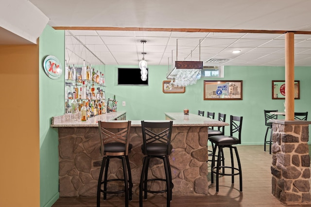 bar with a drop ceiling, visible vents, baseboards, bar, and wood finished floors