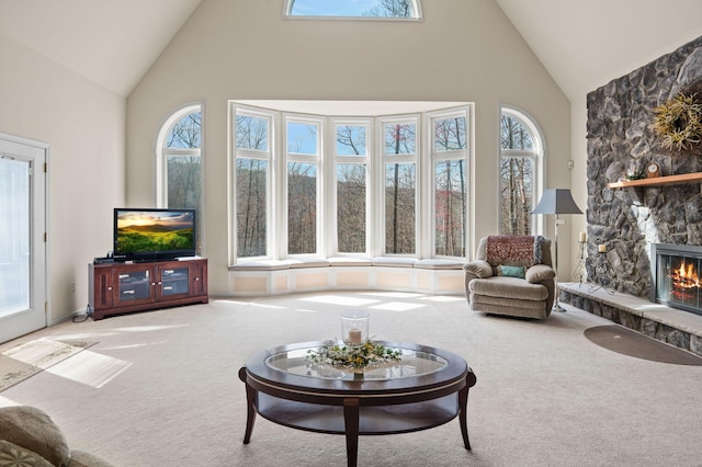carpeted living area with high vaulted ceiling and a stone fireplace