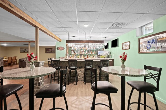 dining room with light wood finished floors, baseboards, visible vents, a bar, and a paneled ceiling