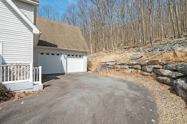 view of side of property with a shingled roof, an attached garage, and aphalt driveway