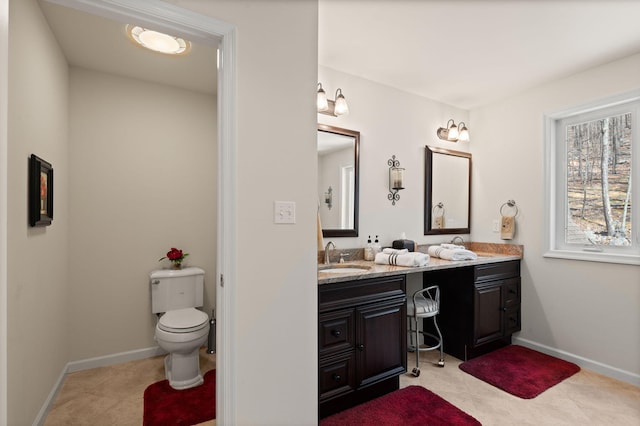 bathroom with double vanity, toilet, baseboards, and a sink