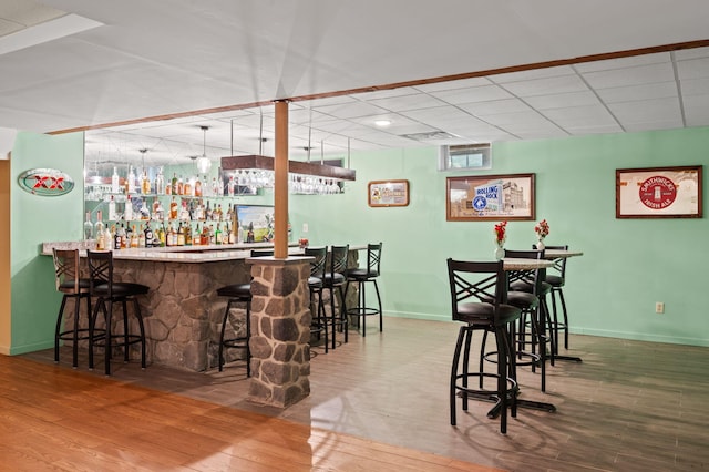 bar with baseboards, wood finished floors, a dry bar, and a paneled ceiling