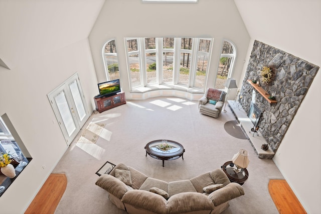living room with high vaulted ceiling, a stone fireplace, and carpet