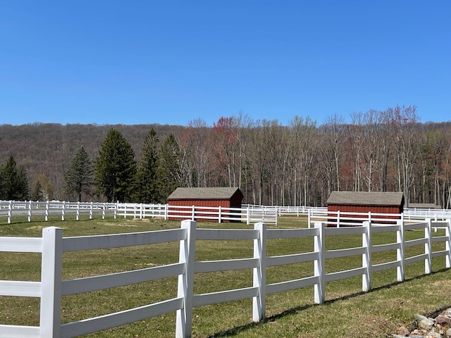 view of yard featuring an outdoor structure, a rural view, a wooded view, a storage unit, and fence