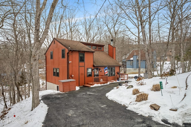 view of front of home with a deck, roof with shingles, and a chimney