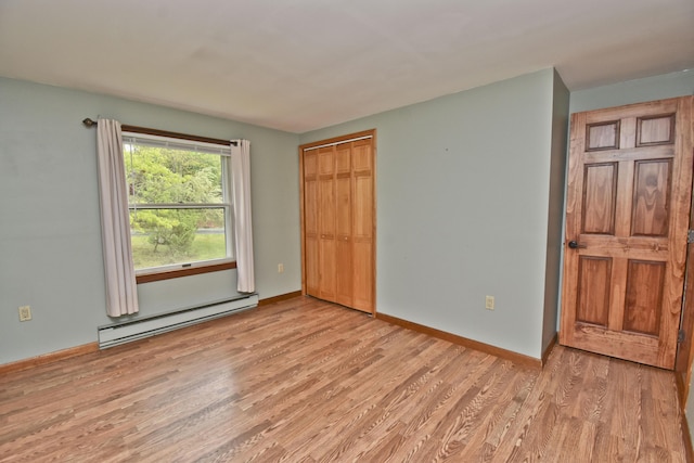 unfurnished bedroom featuring a baseboard heating unit, light wood-style floors, a closet, and baseboards