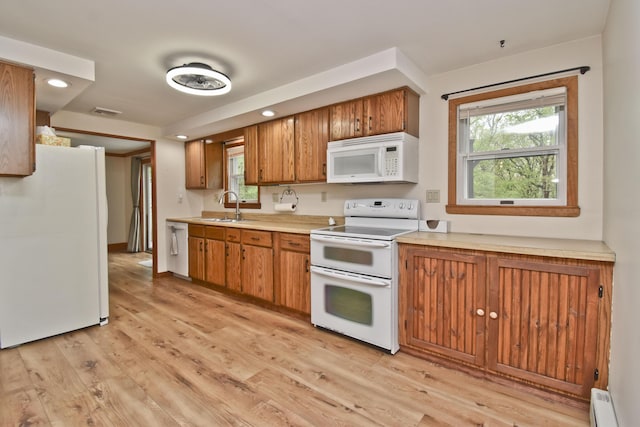 kitchen featuring white appliances, a sink, brown cabinetry, light countertops, and light wood finished floors