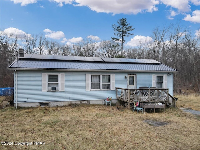 rear view of property featuring metal roof, a yard, solar panels, and a deck