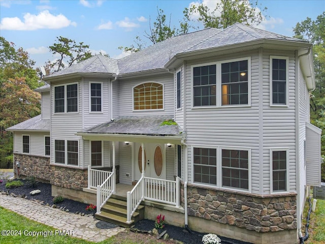 view of front of property with covered porch, stone siding, and a shingled roof