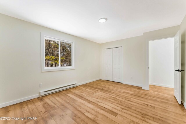 unfurnished bedroom featuring baseboard heating, a closet, and light wood-type flooring