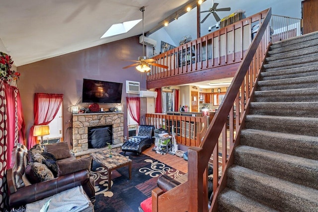 living area with a ceiling fan, a wall mounted AC, wood finished floors, a stone fireplace, and stairs