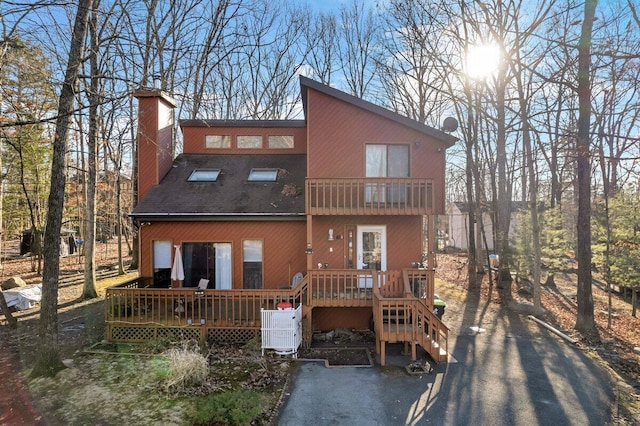 back of house with a wooden deck, driveway, a chimney, and a balcony